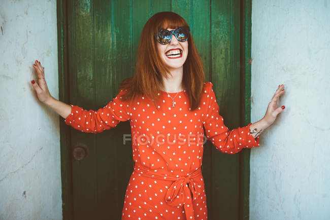 Rindo menina ruiva em óculos de sol posando na porta — Fotografia de Stock