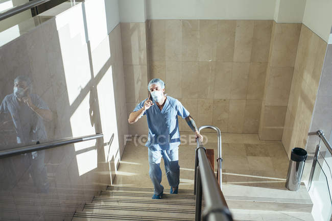 Homem de uniforme médico falando ao telefone e subindo escadas no hospital — Fotografia de Stock