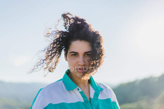 Sinnliches Mädchen mit kurvigen Haaren posiert im Sonnenlicht und blickt in die Kamera — Stockfoto