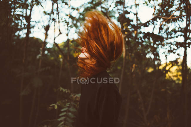 Vista lateral de mujer pelirroja agitando el pelo en el fondo de la naturaleza - foto de stock