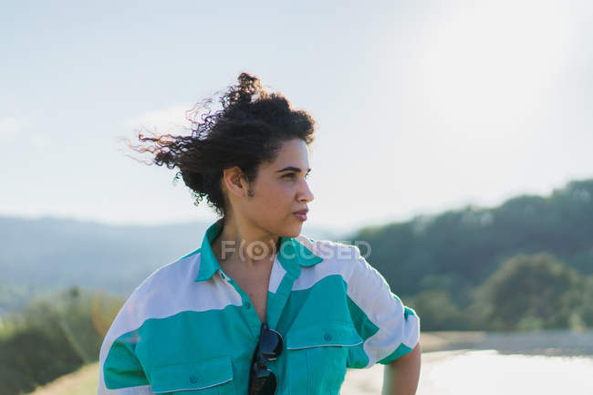Кудрявая женщина позирует на природе в солнечном свете и смотрит в сторону — стоковое фото