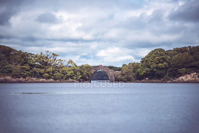 Distant view of small arch bridge connecting two shores of river — Stock Photo