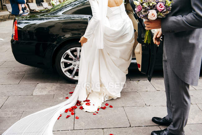 Vista trasera de la novia en vestido blanco entrar en el coche - foto de stock