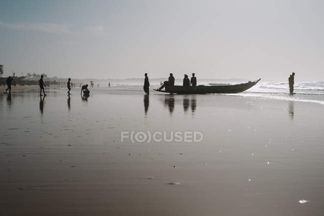 Goree, senegal- 6. Dezember 2017: Silhouetten afrikanischer Menschen, die abends auf einem Boot am Sandstrand stehen. — Stockfoto
