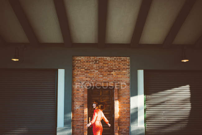 Femme rousse élégante en rouge tournant autour de la porte en plein soleil . — Photo de stock