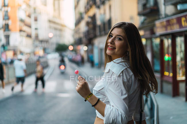Bruna donna con lecca-lecca guardando sopra la spalla alla macchina fotografica — Foto stock