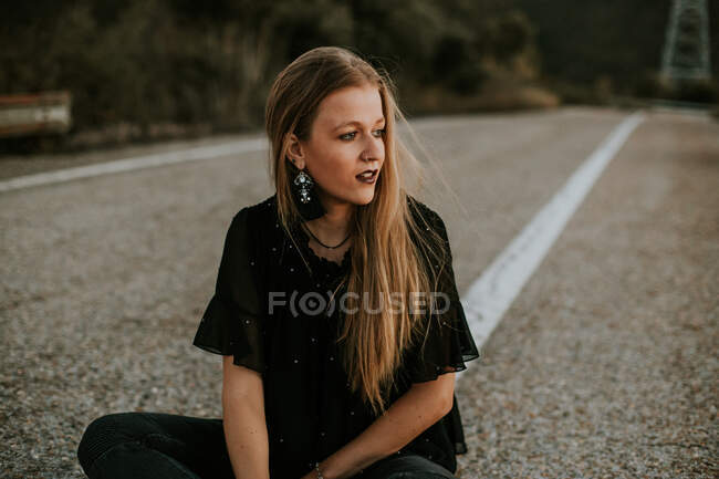 Стильная молодая женщина сидит на обочине дороги — стоковое фото