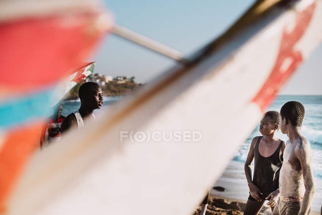 Гори, Сенегал - 6 декабря 2017 года: Загадочный взгляд двух мальчиков, слушающих молодого человека, стоя на пляже в солнечный день . — стоковое фото