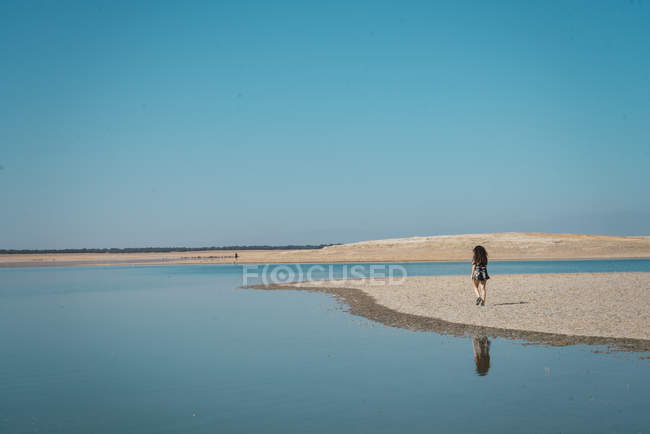 Силуэт женщины, идущей по берегу бирюзового озера — стоковое фото