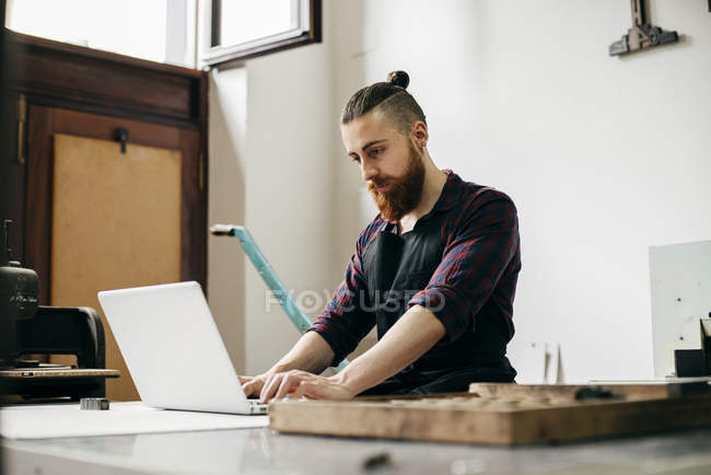 Hombre escribiendo en el ordenador portátil en la mesa del taller - foto de stock