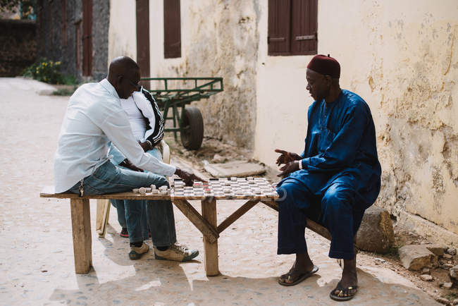 Yoff, Senegal- December 6, 2017: Side view of two African men sitting on street and playing checkers — Stock Photo