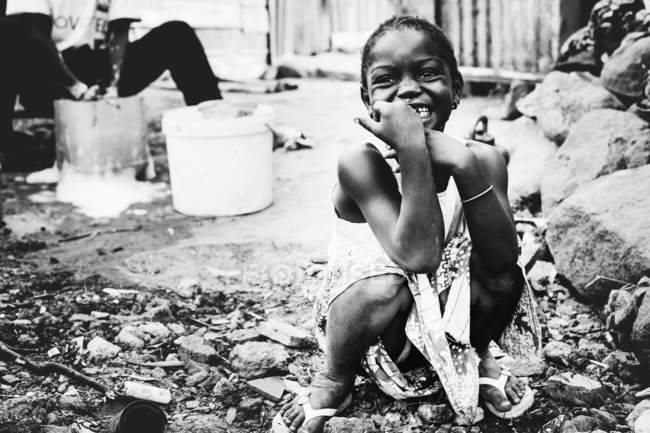 Senegal- 6. Dezember 2017: Lächelndes Mädchen sitzt auf schmutziger Straße und schaut weg. — Stockfoto