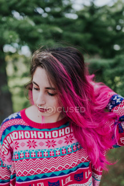 Bonita chica en jersey caliente ajustando el pelo rosa y mirando hacia abajo - foto de stock