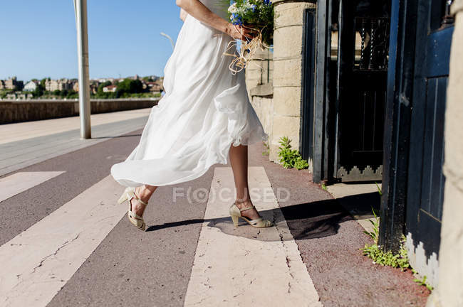 Low section of bride in light dress holding bright bouquet and entering church. — Stock Photo