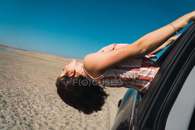Side view of woman hanging out of riding in desert car window — Stock Photo