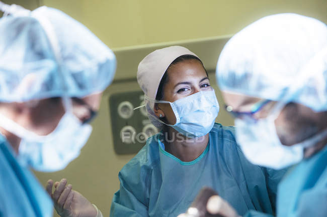 Lachende Frau in Chirurgenuniform schaut Ärzte im Operationssaal an — Stockfoto
