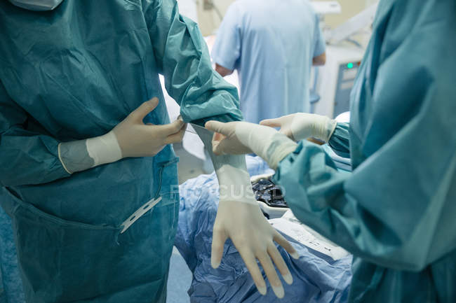 Hände, die dem Arzt helfen, vor der Operation die Uniform anzuziehen. — Stockfoto