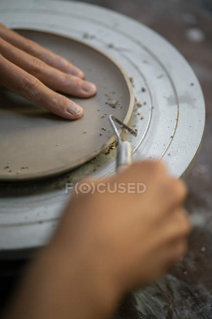 Imagen de las manos de alfarero hembra moldeando el borde de la placa de arcilla con instrumento - foto de stock