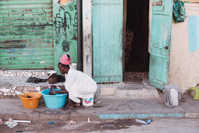 Goree, Senegal- 6 dicembre 2017: Vista laterale della donna africana seduta vicino alla sua casa e che lava la biancheria nel bacino di plastica . — Foto stock