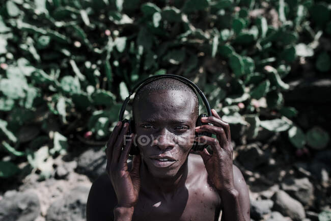 Portrait de l'homme impressionné africain écoutant de la musique dans les écouteurs et regardant la caméra. — Photo de stock