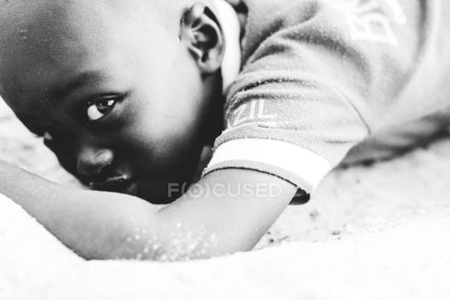 Yoff, Senegal- December 6, 2017: Crop African boy lying on sand and looking at camera. — Stock Photo