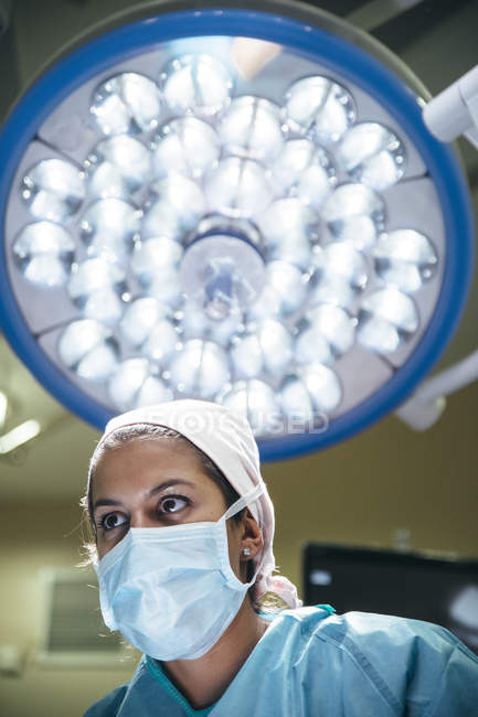 Высокоугловой портрет женщины-хирурга в маске на фоне хирургической лампы — стоковое фото