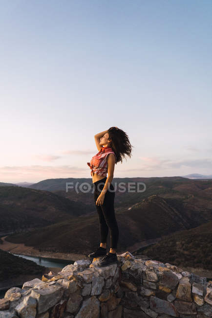 Стильна дівчина з пишним волоссям позує на терасі з краєвидом на гори — стокове фото