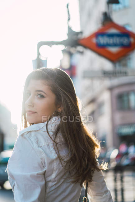 Brunette fille en vêtements décontractés regardant par-dessus l'épaule à la caméra près de métro — Photo de stock