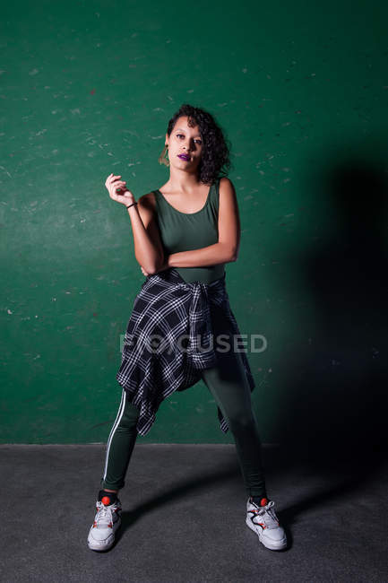 Портрет городской танцовщицы, позирующей над зеленой стеной и смотрящей в камеру — стоковое фото