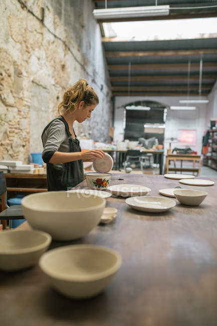 Side view of female potter in apron creating plates from white clay. — Stock Photo