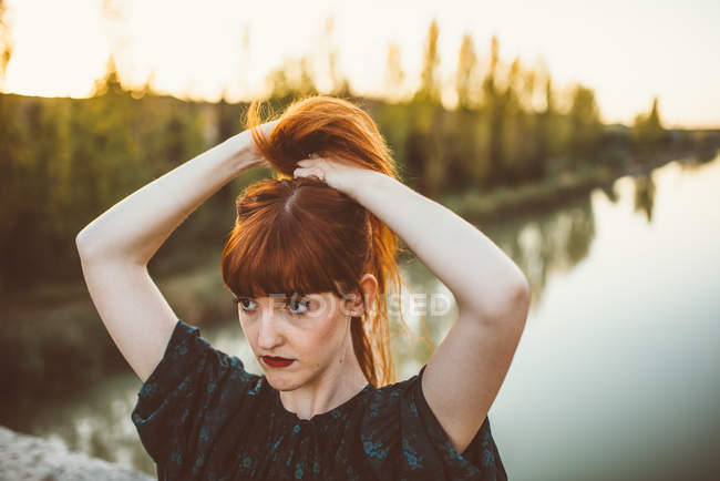 Portrait of ginger woman collecting hair pony tail on rural bridge in sunlight — Stock Photo
