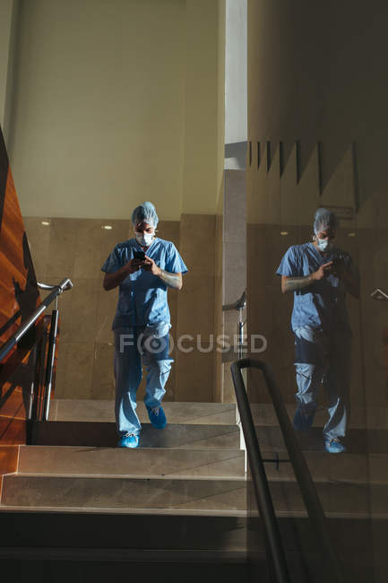 Surgeon walking in hospital hall browsing phone — Stock Photo