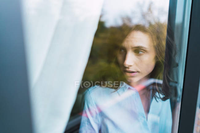 Mulher morena bonita em pé atrás do vidro da janela — Fotografia de Stock