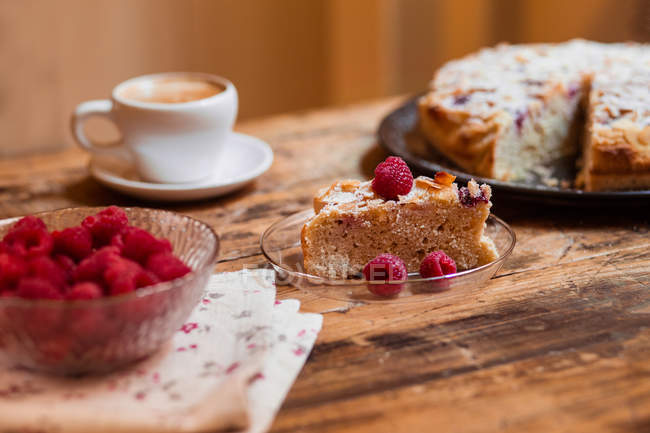 Slice of raspberries cake with almonds  by cup of coffee on wooden table — Stock Photo