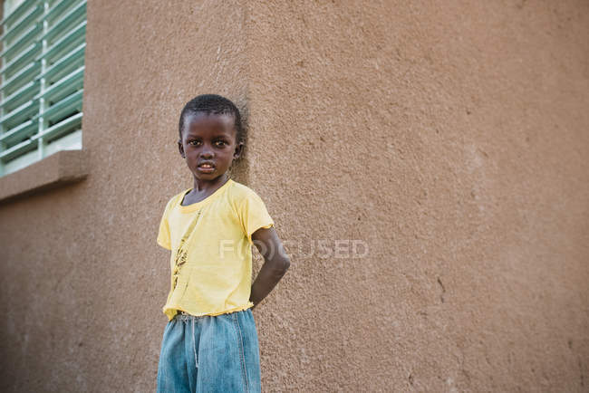 Yoff, senegal- 6. Dezember 2017: Porträt eines kleinen schwarzen Jungen, der an einer Mauer an der Straße lehnt — Stockfoto