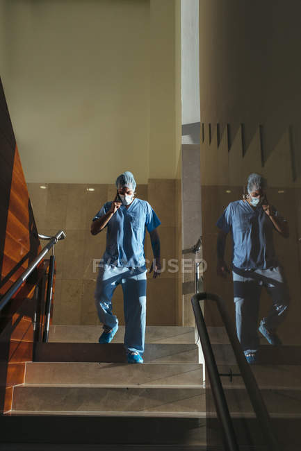 Blick aus der Vogelperspektive auf einen Arzt, der telefoniert, während er im Krankenhaus die Treppe hinuntergeht — Stockfoto