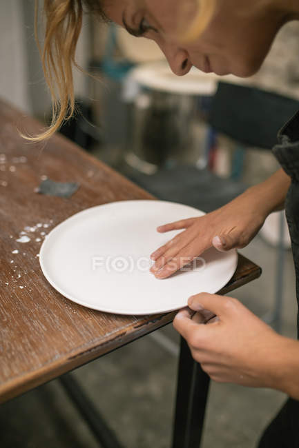 Retrato de mujer concentrada inclinándose sobre la placa y formándola de arcilla blanca . - foto de stock