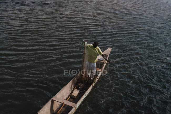 Goree, Senegal- Dezembro 6, 2017: Vista de baixo ângulo do homem de pé em barco de madeira e segurando rede de pesca . — Fotografia de Stock