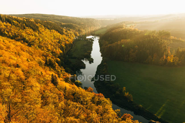 Increíble paisaje del valle del río con árboles dorados en la pendiente de las colinas - foto de stock