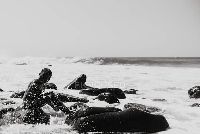 Goree, senegal- 6. Dezember 2017: lachendes Kind sitzt auf Felsen der Küste in Tropfen von Wellen. — Stockfoto