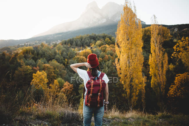 Vista posteriore della donna che indossa lo zaino che regola il cappello rosso sulla scena della natura — Foto stock