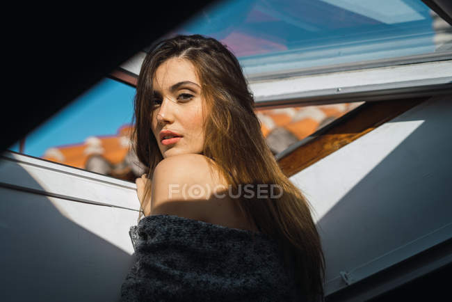 Brunette woman posing in window and looking over shoulder at camera — Stock Photo