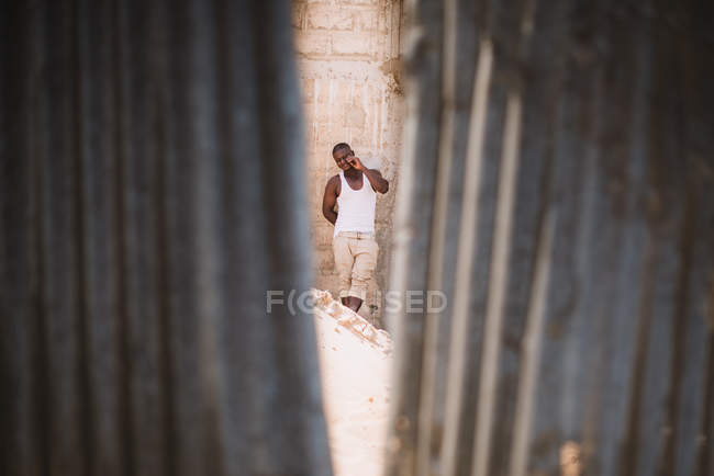 Goree, Senegal- 6 dicembre 2017: Girato attraverso la crepa nel muro di un uomo africano occasionale in piedi sulla strada e che fa gesti alla telecamera . — Foto stock