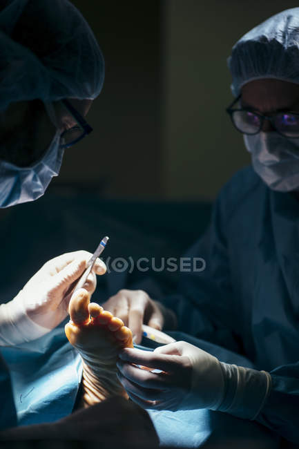 Vista de cerca de los médicos en uniforme explorando el pie del paciente mientras realiza la cirugía . - foto de stock