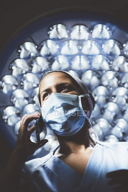High angle view of surgeon in uniform talking on smartphone over lamp on background — Stock Photo