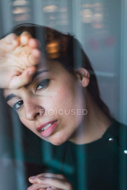 Portrait of young brunette posing sensually behind window and looking at camera — Stock Photo