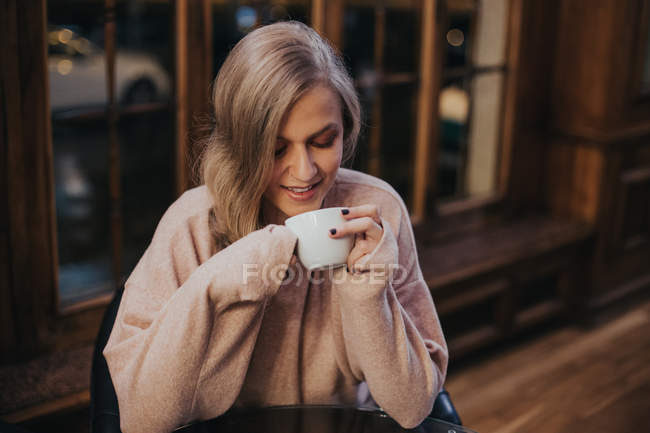 Mujer sentada barra contador y buscando en taza blanca - foto de stock