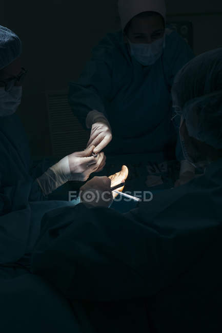 Groupe de chirurgiens opérant le patient dans une tache lumineuse — Photo de stock
