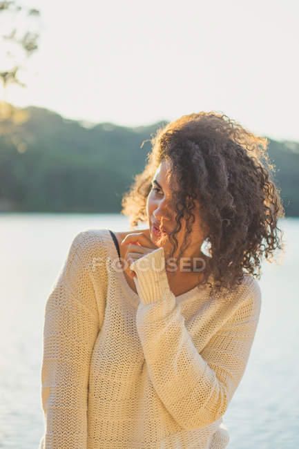 Весела жінка в білому светрі позує на озері — стокове фото