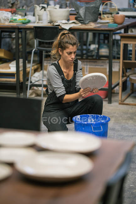 Frau hockt mit Tonteller über Eimer in Werkstatt — Stockfoto